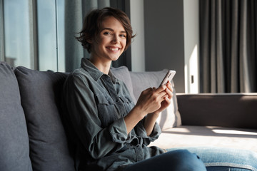 Image of beautiful young joyful woman using mobile phone and smiling