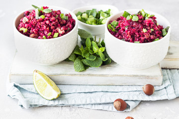 White ceramic bowls with warm buckwheat, beetroot, nuts and herbs salad on wooden board, light grey concrete background. Dietary balanced food. Vegetarian and vegan concept. 