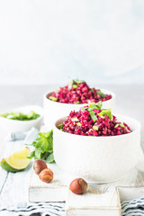 White ceramic bowls with warm buckwheat, beetroot, nuts and herbs salad on wooden board, light grey concrete background. Dietary balanced food. Vegetarian and vegan concept. 