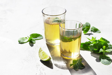 Moroccan tea with mint leaves and lime, light grey concrete background. Trendy style with artistic shadows.