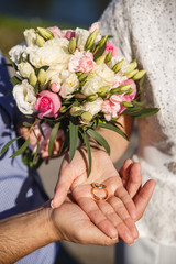 Obraz na płótnie Canvas Hands of newlyweds with wedding rings lying on their palms and a wedding bouquet of flowers. Concept of wedding love and Valentine's Day.