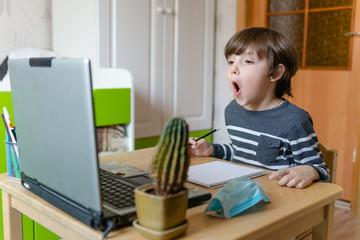 Distance learning for children during the coronavirus epidemic. A boy sits at a table and performs...
