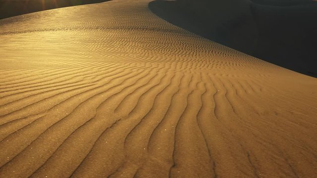 Sand dune with a pattern in the sunset sun rays in a desert. Sand grains gliterring. Camera moving sideways. UHD