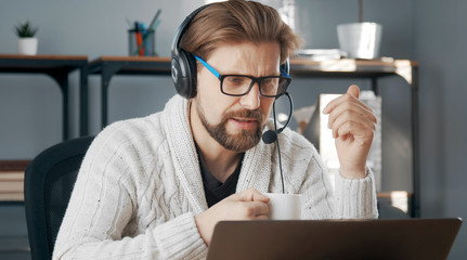 Casual-dressed male with headset teleworking sitting in front of computer, isolation due to epidemic