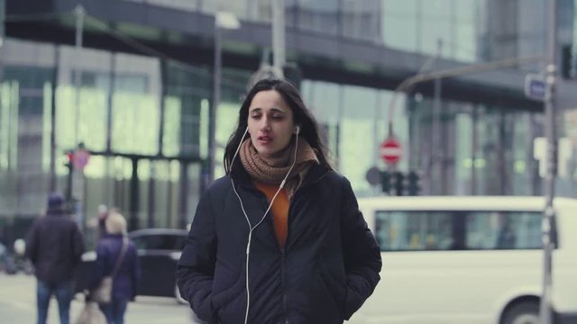 Young Woman Listening to Earphones on City Street Background