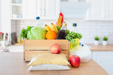 A wooden box of different food, fruit, vegetables, oil, water, sugar on the kitchen. Safe home delivery.