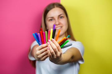 Beautiful young girl in a white T-shirt holds multicolored felt-tip pens for drawing