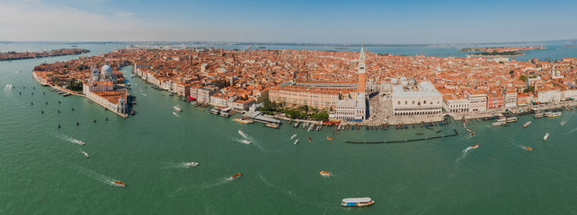 Aerial panoramic shot of Venice city and Grand Canal, Italy. View from above. Tiled roofs and nerros streets. Venetian atmosphere. Blue sky and lagoon water. Historical buildings. © Artem