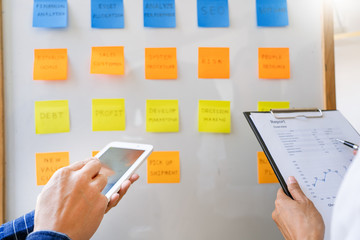 Business people arranging sticky notes commenting and brainstorming on work priorities colleague in a modern co-working space.