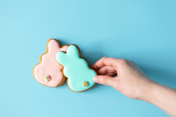 Woman takink Easter cookies rabbit shape on blue background with copy space, top view