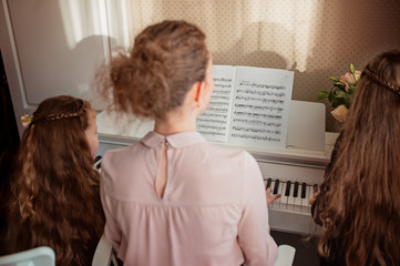 Home piano lesson. A woman and two girls practice sheet music on one musical instrument. Family concept. The idea of activities for children during quarantine.