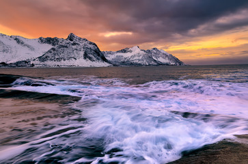 Fototapeta na wymiar View over Ersfjord from colorful rocks at sunset and rockpools to snowy mountains on a dark cloudy day, Cape Tungeneset, Senja, Norway. Europe. Long exposure shot
