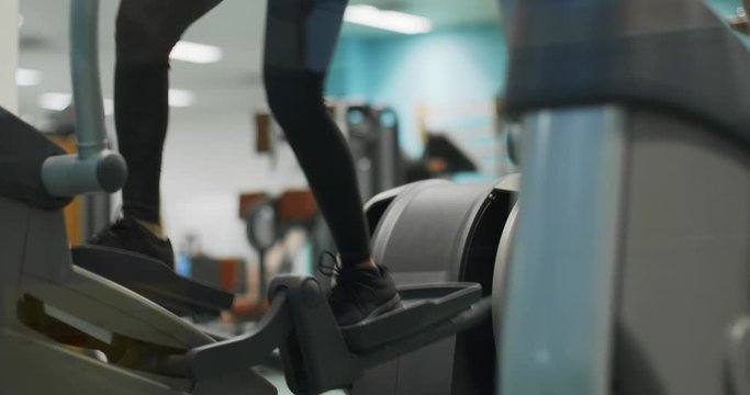 woman exercising with elliptical walking machine at gym.Front view legs walikng detail, slow motion. Woman training on machine. Woman walking on gym machine