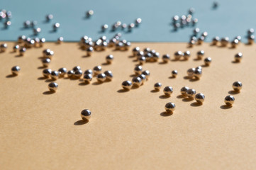 Macro silver bakery beads with sunny shadows, sugar pearls on the light yellow and blue background, color of ukrainian flag. Trendy concept idea