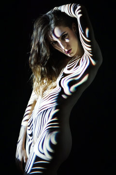 Young woman in studio with artistic projection from slide projector looks as if she was painted with body painting