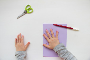 Child made a greeting card. Step 4. Child holds a card in his hands. Tools and materials for children's art creativity on table. Mother's day or March 8 greeting card DIY idea. 