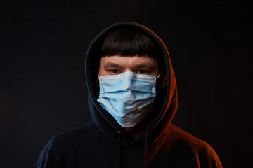 portrait young guy in black hoodie on medicine mask on black background