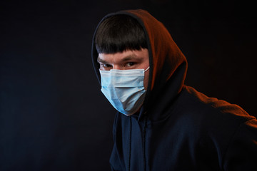 portrait young guy in black hoodie on medicine mask on black background