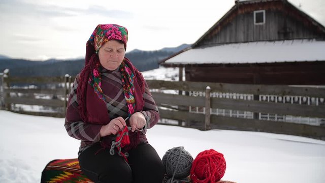 Old lady knits near house at winter, carpathian mountains, ukraine