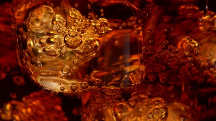 Ice cubes with bubbles in a rotating glass of cola. Abstract super close-up shot, UHD