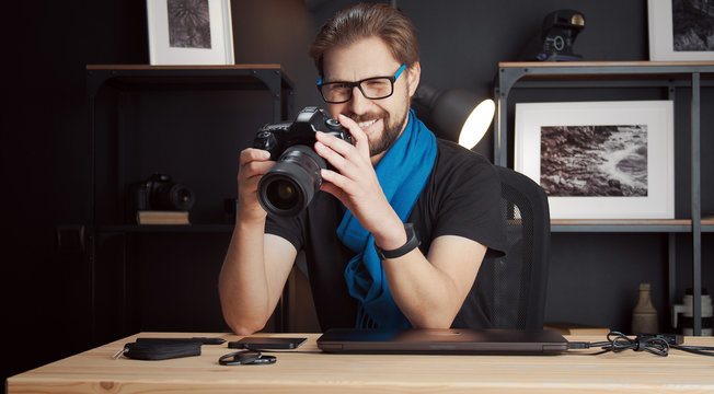 Adult smiling photographer reviewing captured photos in DSLR camera sitting at desk in studio