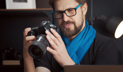 Close-up of joyful mature male photographer reviewing pictures in DSLR camera staying in studio