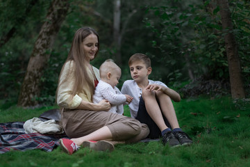 Naklejka na ściany i meble Family picnic at garden park outdoors. Mother, eldest son and youngest child sitting on picnic blanket