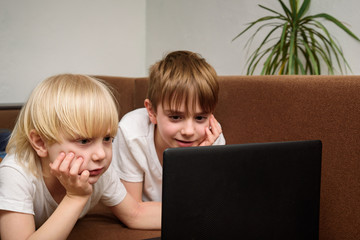 Children look at laptop screen resting his face with his hand. Friends teenagers watching movie