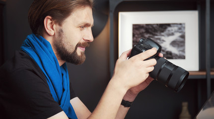 Cropped shot of satisfied adult photographer reviewing taken images in DSLR camera holding it in hands