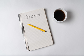 Top view of notepad with inscription Dream. Pen and cup of coffee. Motivational note