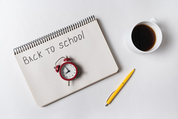 Inscription in copybook BACK TO SCHOOL. Vintage alarm clock and cup of coffee