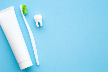 White tooth, tube of toothpaste and toothbrush with green bristles on pastel blue table background. People teeth hygiene. Empty place for text, quote, sayings or logo. Closeup. Top down view. 