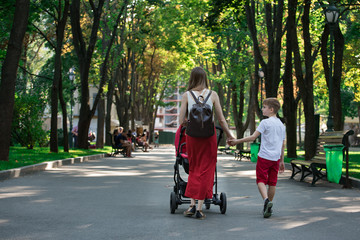 Fototapeta premium Mom walks in the Park with stroller and elder son. Walk with children. Childhood Lifestyle