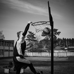 Young man jumping and making a slam dunk playing streetball. Black and white