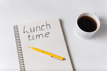 Notebook with LUNCH TIME inscription. Cup of coffee and pen white background