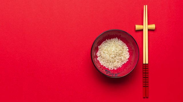 Rice Bowl and Chopsticks on Red Background. Stop Motion Time Lapse in 4K. Product Presentation Mockup or Template.Top Down View with Copy Space.