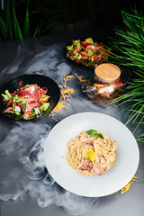 Pasta carbonara, vegetable salad with prosciutto and vegetable salad with salmon on a gray-smoked background