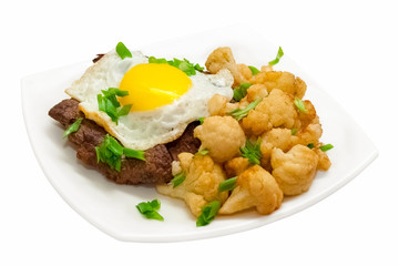 Beef steak with fried eggs with a side dish of fried broccoli on a white plate. Isolated object