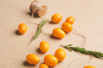 Tasty kumquat fruit with rosemary and thread on color background
