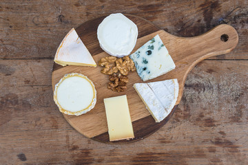 Various of traditional french cheeses and nuts on wooden cutting board top view