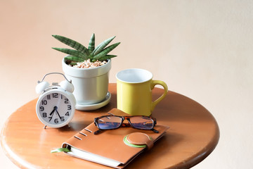 Sansevieria Boncel, alarm clock, yellow mug, notebook and eye glasses on wooden table with morning sunlight,morming routine, self isolation, quarantine concept.