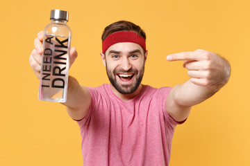 Funny young bearded fitness sporty guy sportsman in headband t-shirt spend weekend in home gym isolated on yellow background. Workout sport motivation concept. Pointing index finger on water bottle.