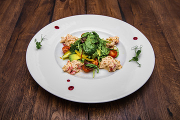 Crab and avocado salad with cherry tomatoes, mixed salad with cherry sauce. On a wooden table.