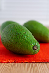 Close-up of green avocados, with selective focus, on red tablecloth, wooden table and white background, vertical, with copy space