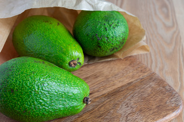 Top view of whole green avocados, with selective focus, in paper bag, on wooden table, horizontal