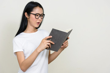 Stressed young Asian woman with eyeglasses reading book and looking shocked