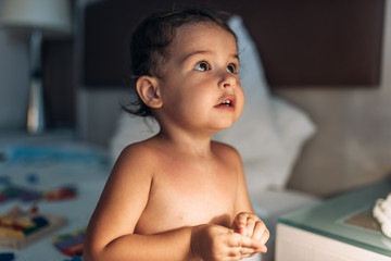 Image of cute baby girl playing with wood colorful toys in the bed on lamplight. Toddler is playing with toy wooden at home. Child playing with colorful toy blocks in white bedroom. Educational game.