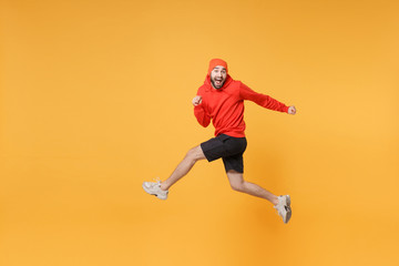 Fototapeta na wymiar Surprised young bearded fitness sporty guy 20s sportsman in hat hoodie shorts spend weekend in home gym isolated on yellow background. Workout sport motivation lifestyle concept. Jumping like running.