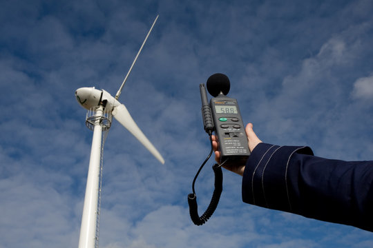A sound meter is held up to a wind turbine to assess noise pollution