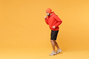 Fototapeta na wymiar Side view of young bearded fitness sporty guy sportsman in hat, hoodie, shorts spend weekend in home gym isolated on yellow background in studio. Workout sport motivation lifestyle concept. Running.